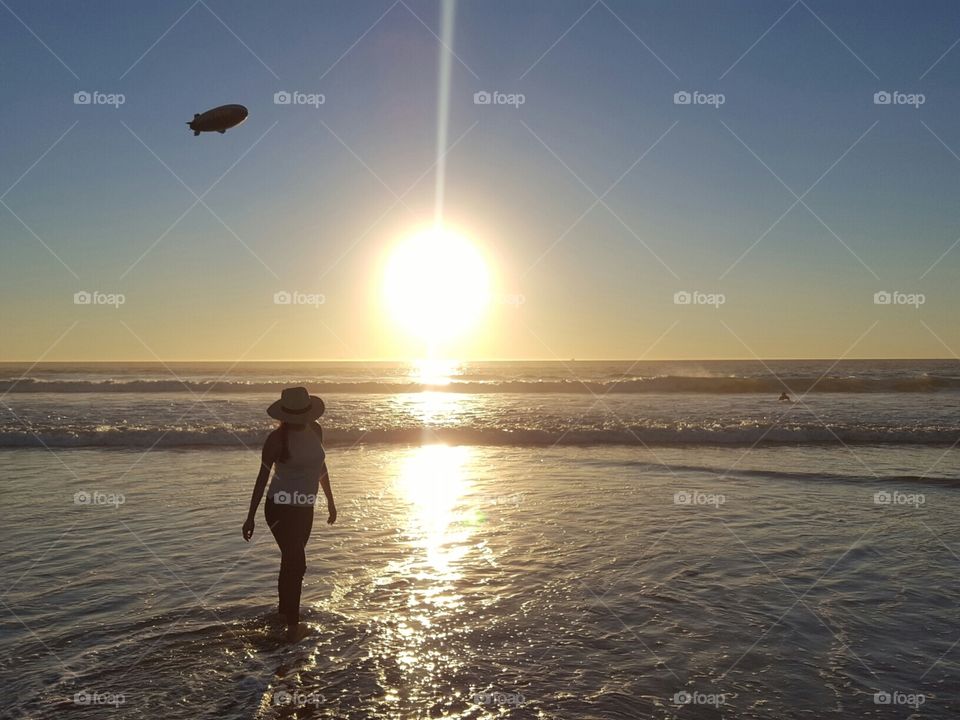 Silhouette of a young woman walking along the coast at high tide on the shore of Long Beach, California in winter at sunset