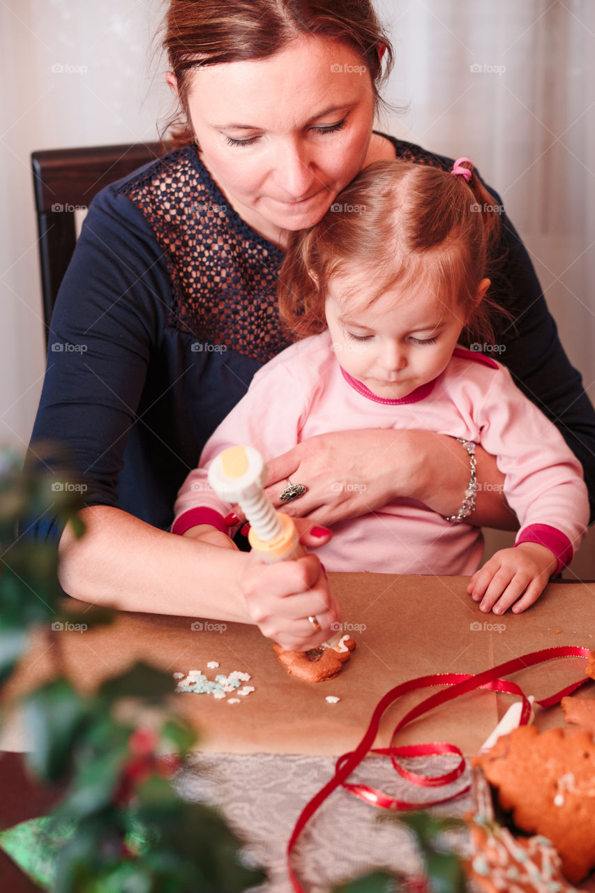 Woman decorating baked Christmas gingerbread cookies with frosting with her little daughter