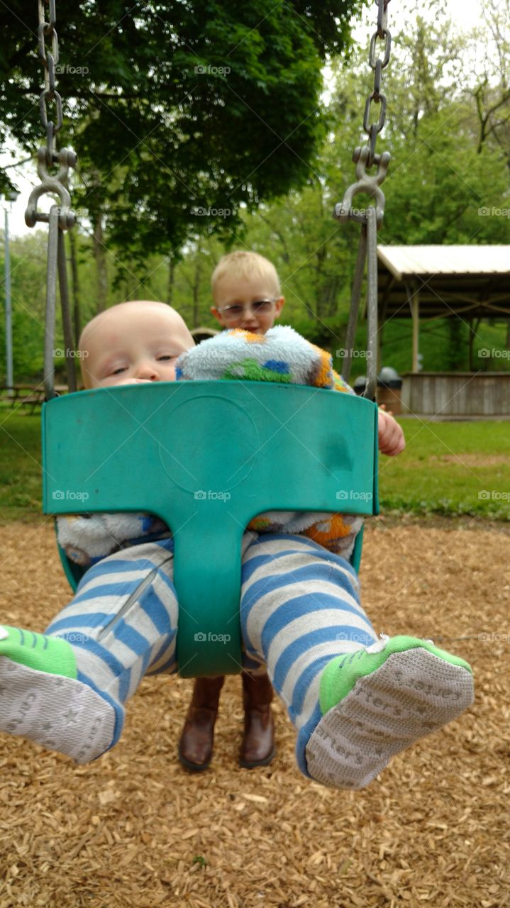 Babyin a swing being pushed by his brother