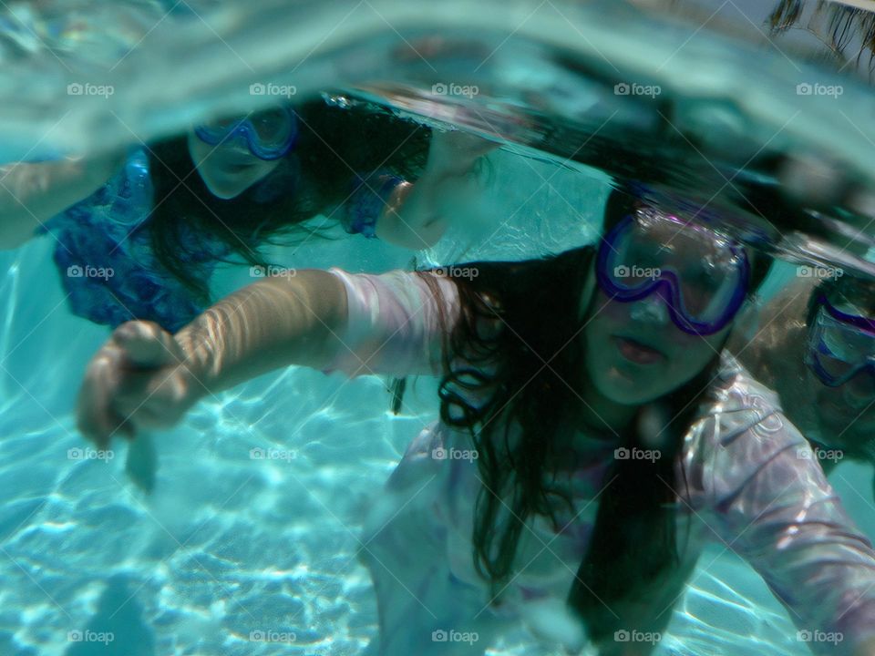 Family under water with dad and daughters happy saying hi making funny faces with goggles on and dress swimsuits and bathing suit with clear water.