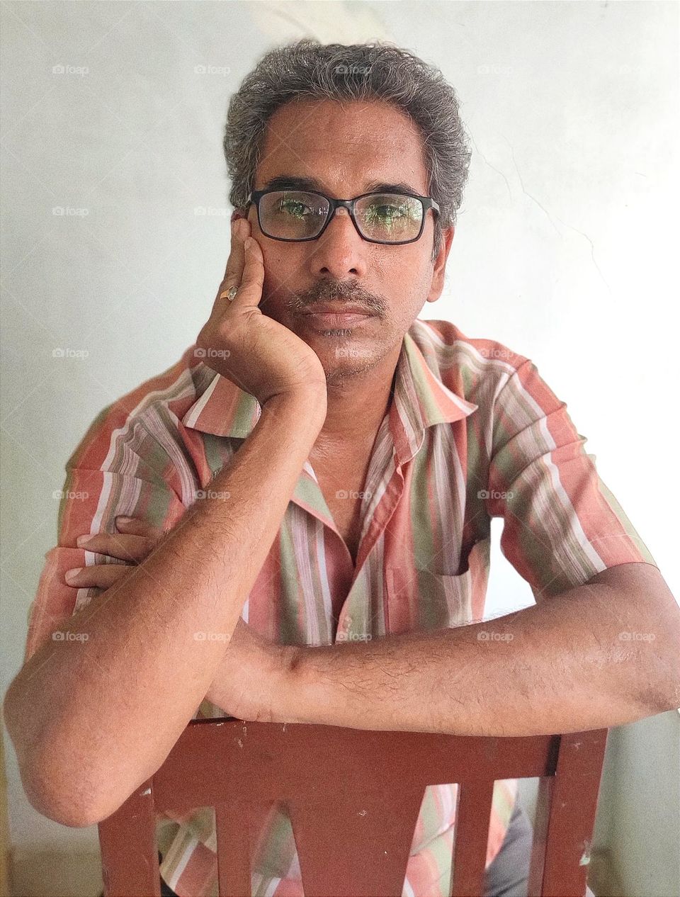 One middle-aged man is sitting with his hands on his cheeks and thinking. The man is wearing glasses.