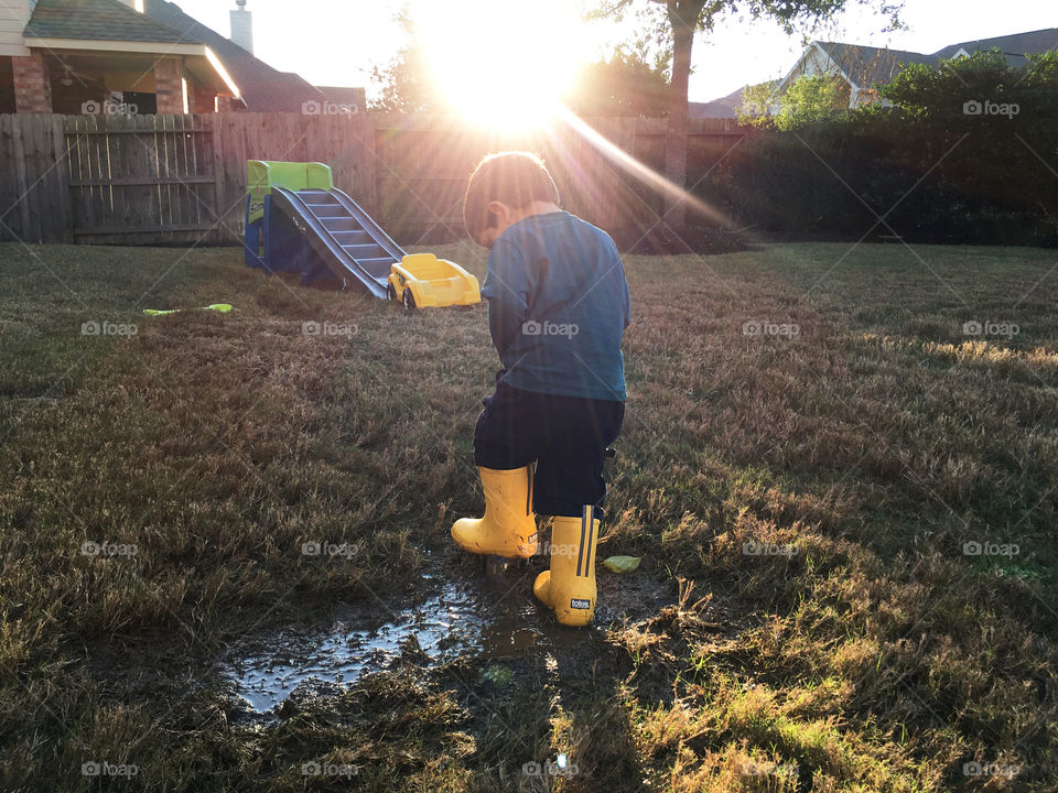 Totes rain boots. Toddler child playing in totes rain boots in backyard mud puddle with sunshine sun rays. Totes cirrus toddler’s charley tall rain boots in yellow.