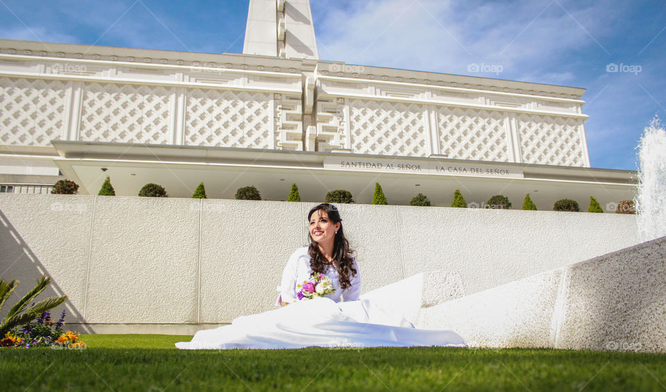 Smiling bride in wedding dress sitting in grass