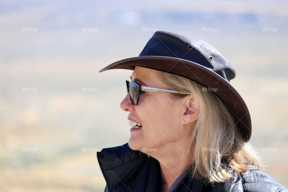 Woman in leather cowboy style hat smiling, headshot profile outdoors 