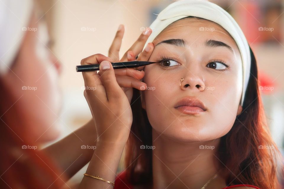 Beautiful teenager girl is putting on an eye liner