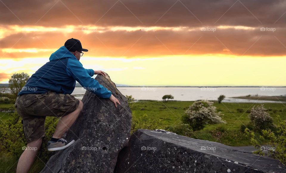 Man climbing on the rock on top of the hill at sunset with stunning view on Corrib lake ,Galway ,Ireland