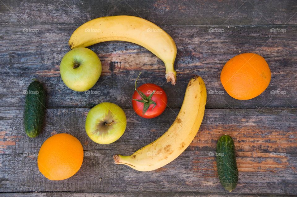 Fresh vegetables and fruits on a wooden table. Tomatoes, cucumbers, bananas, apples and oranges on a wooden background. Flat lay food
