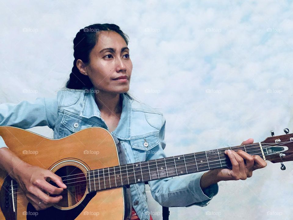 Portrait selfie of a woman playing guitar with clouds background. 