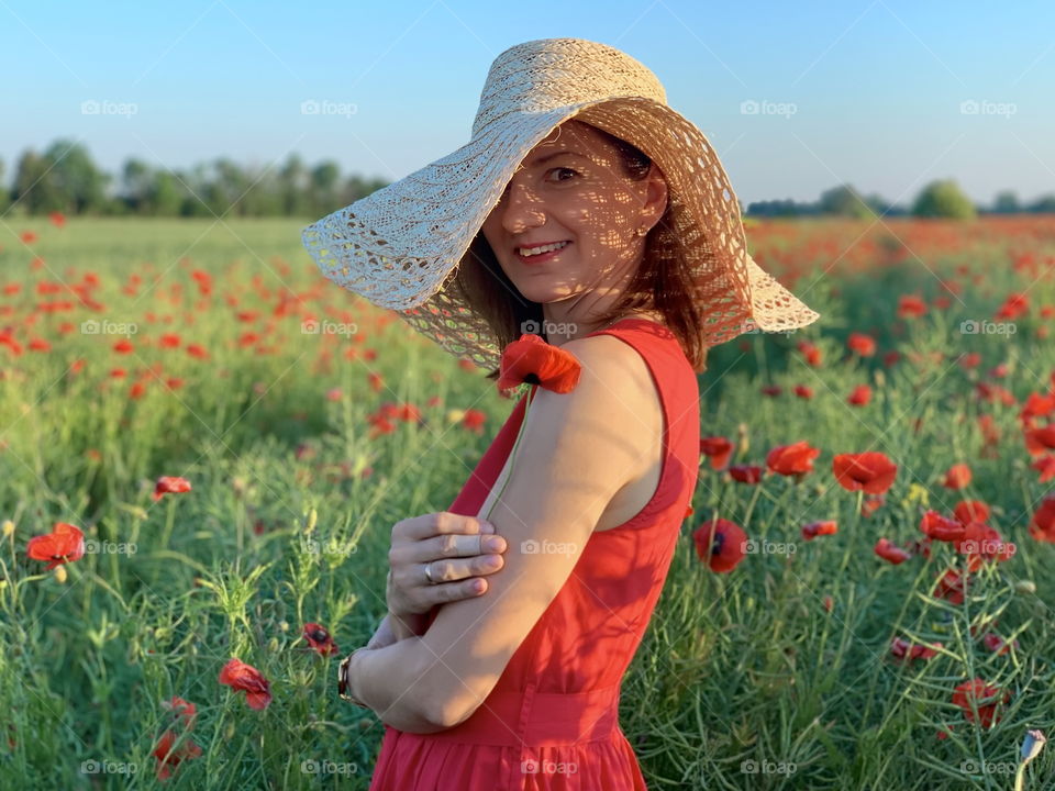 Girl in hat and red dress on the field of poppies