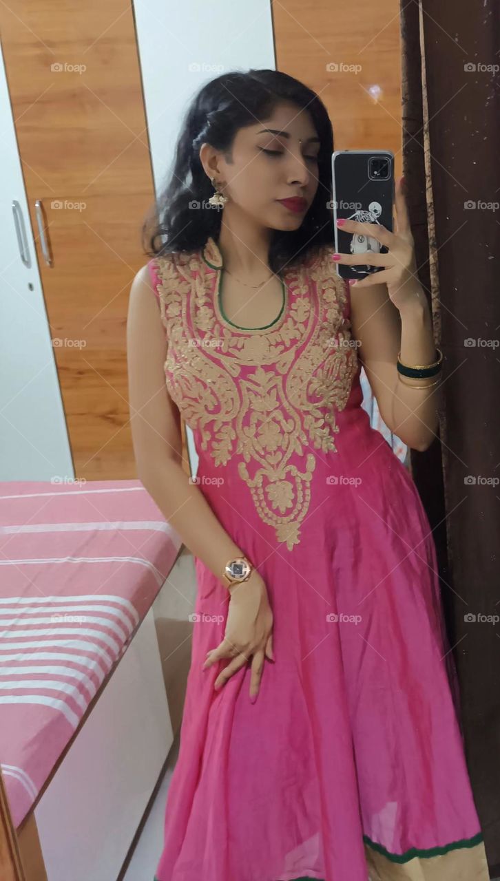 The traditional dress was a stunning ensemble in shades of pink, adorned with intricate golden embroidery that traced elegant patterns along the hem and sleeves. The fabric flowed gracefully, accentuating every movement.