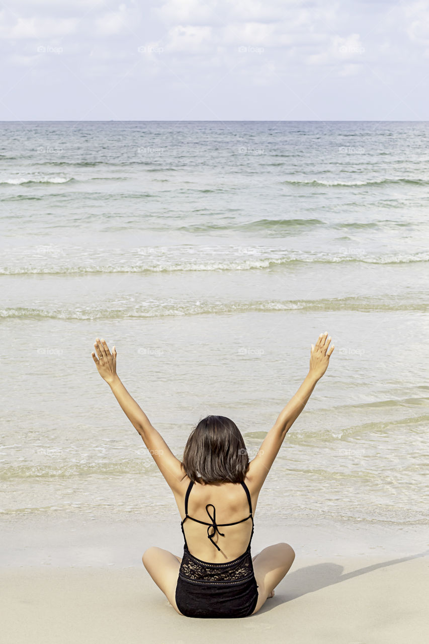 Portrait of Asian woman wearing a swimsuit sitting yoga on the beach background sea and sky