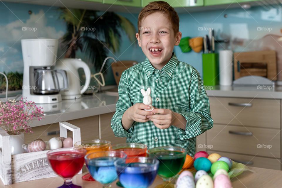 Easte. Redhead boy painting Color eggs and white banny rabbit 