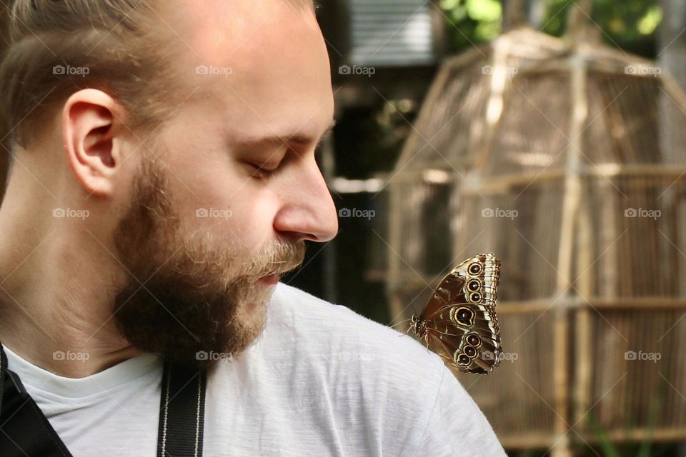 a man with a beard looks at a butterfly on his shoulder