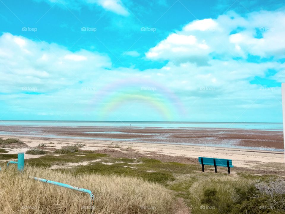 Blue bench on remote beach at low tide, rainbow