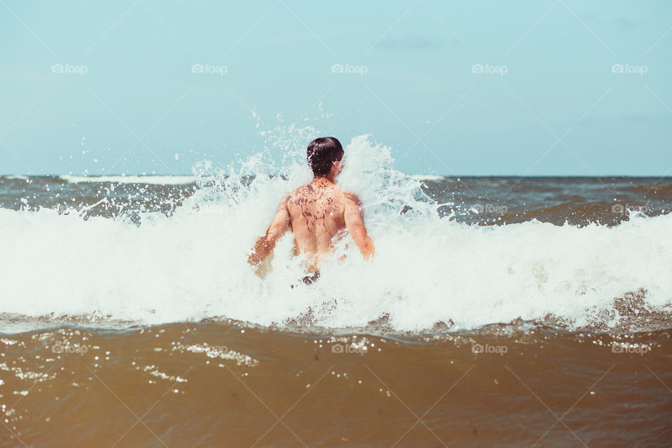 Young man enjoying the high waves in the sea during a summer vacations. Spending a summer holiday by the sea