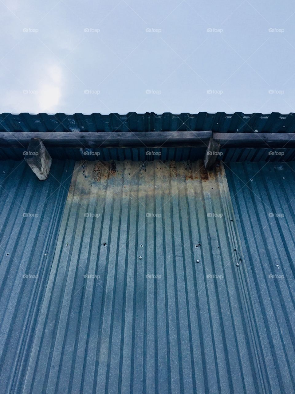 Wooden rafters and overhang of a metal building against a pale blue sky