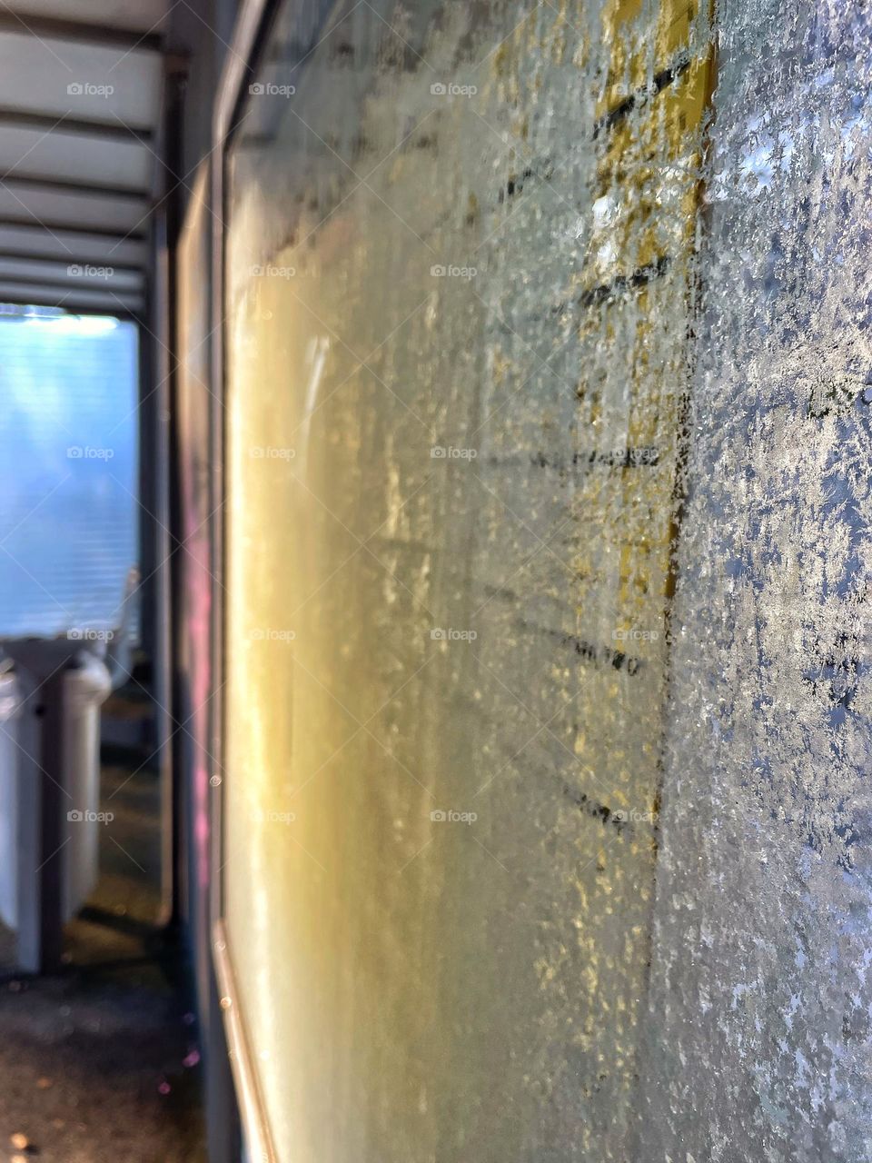 Frozen glass pane with ice crystals and illegible bus timetable at a stop