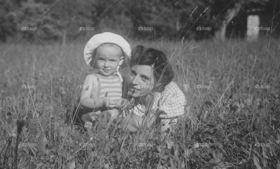 Black and white vintage shot of a woman kneeling in a meadow next to her child in 1947