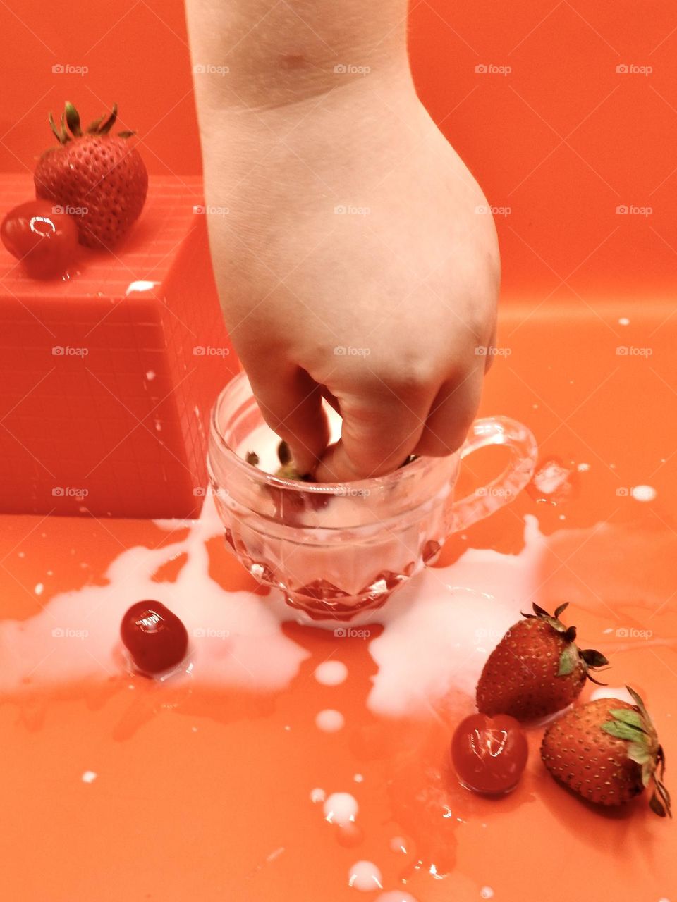 Fall color chosen in red with red background and block with strawberries and cherries with a strawberry that is being picked up from it in the milk in the small glass cup.