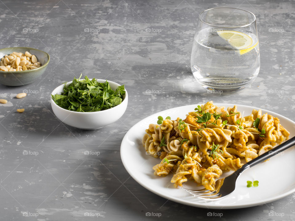 Pasta with curry sauce, served with greens and a glass of water on the grey table