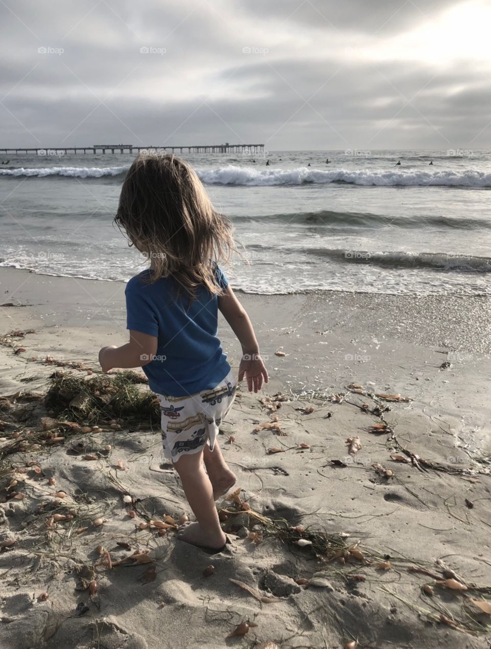 A young child along the edge of the water on a sandy beach, soft color tones from a cloudy day