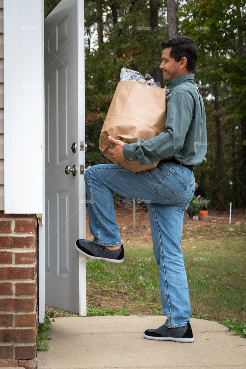 Foap, Routine and Habits of a Daily Life: A man struggles to open the door with his foot as both arms are full of groceries. 