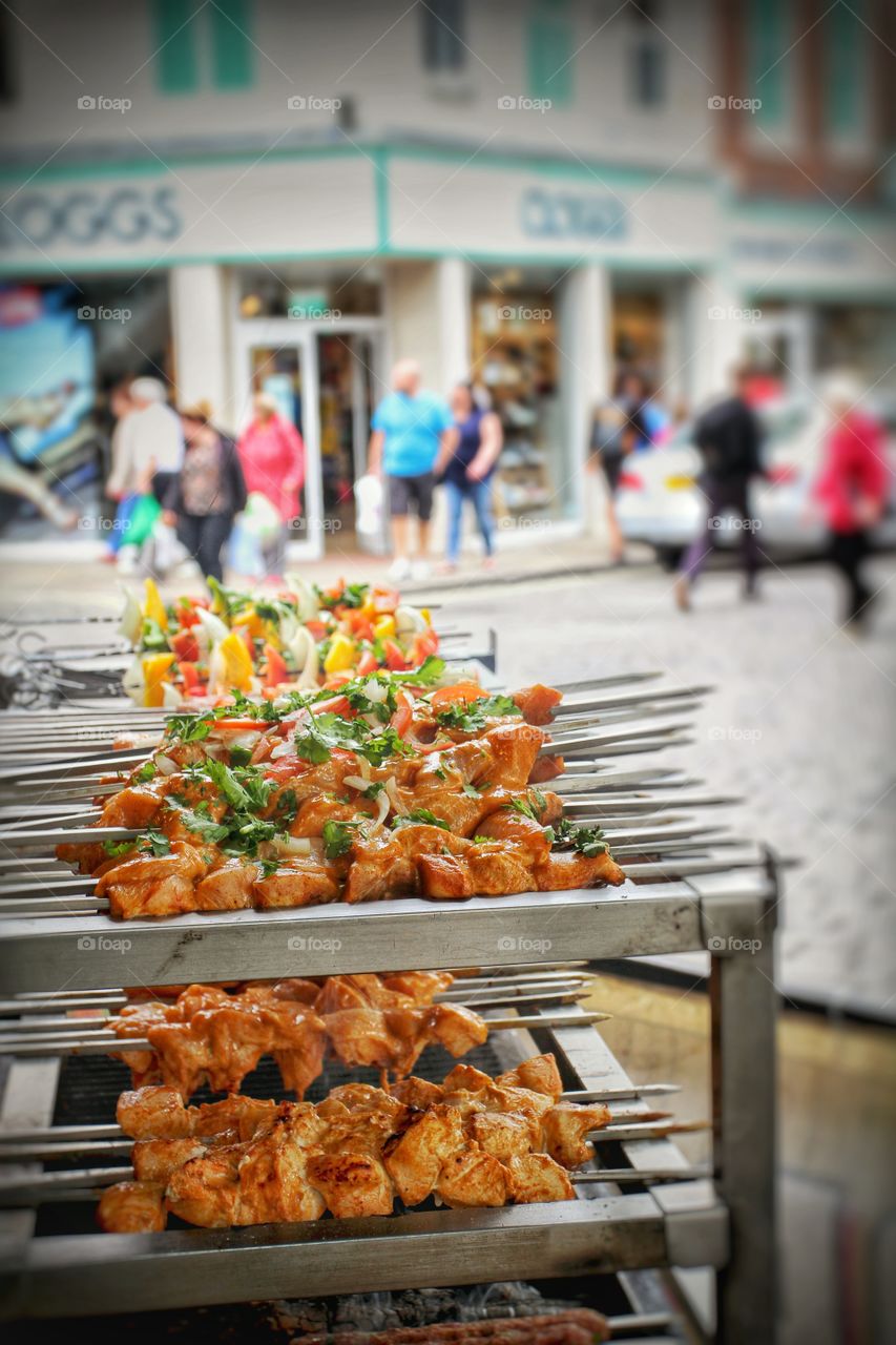 Rows of meaty kebabs grilling on the barbecue of a street food market stall.