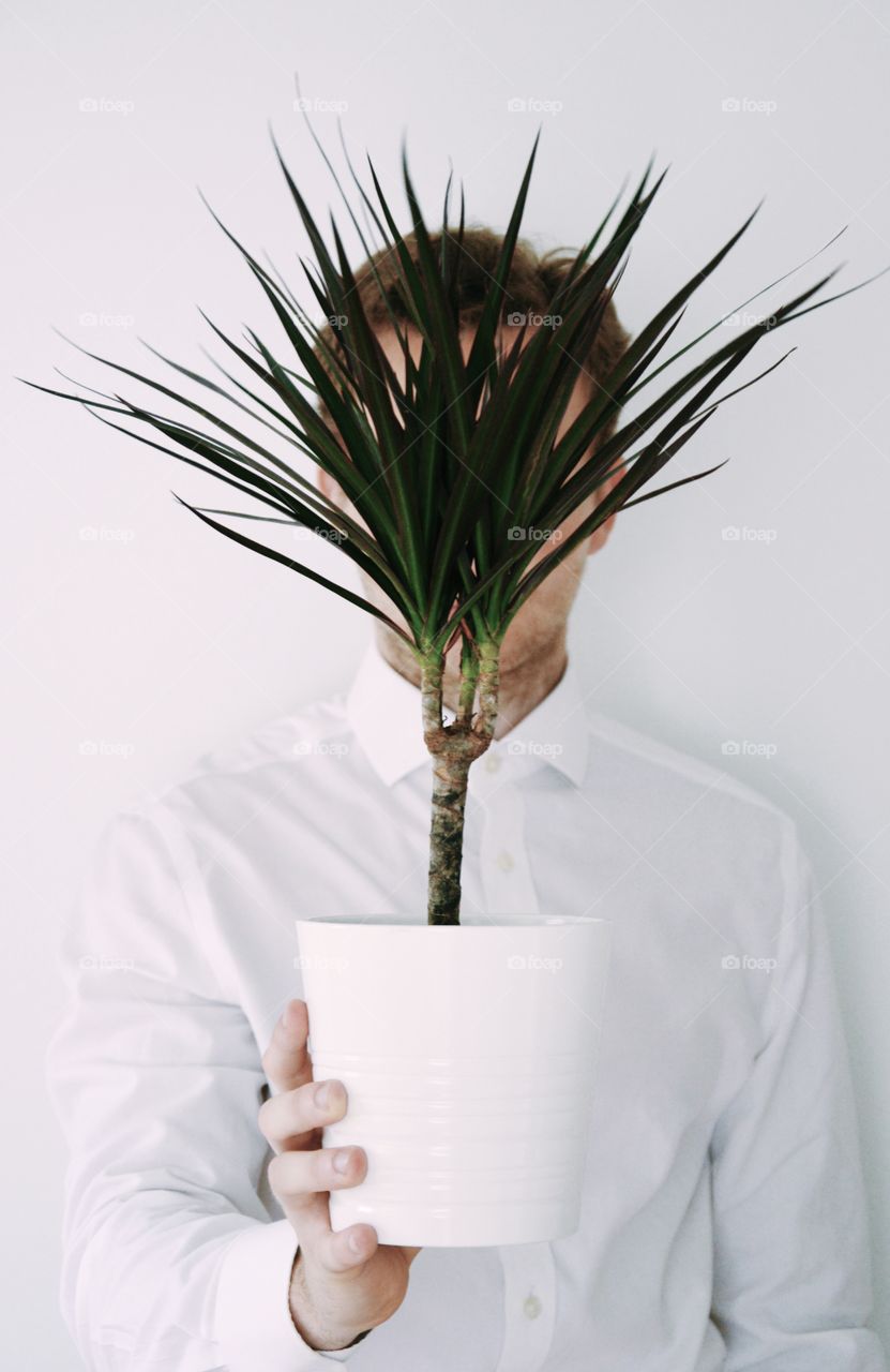 Portrait of a young man holding a plant in front of his head