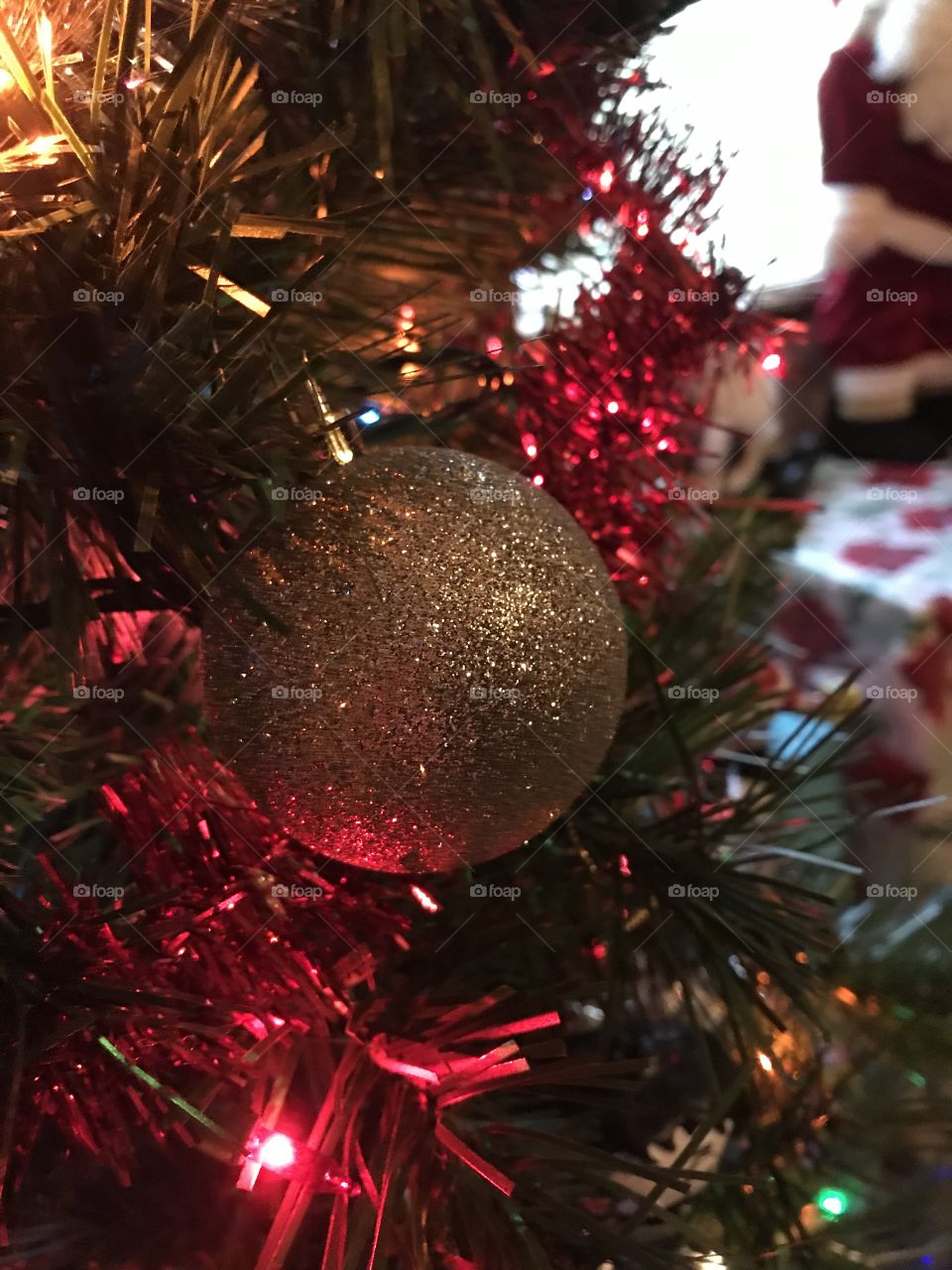A beautiful, sparkling gold Christmas ornament against red tinsel and a green tree. 