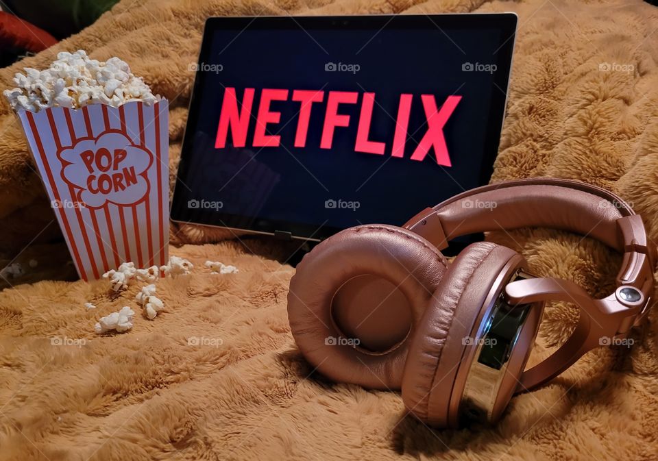 Laptop computer screen ready to watch Netflix for a fun, cozy, and relaxing night with popcorn as a snack, on soft bed blanket in room, with pink headphones