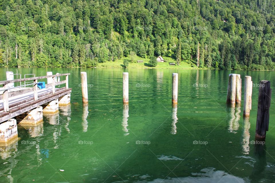 the view from the old pier to the lake with green water against the background of the mountain overgrown with trees and bushes.
