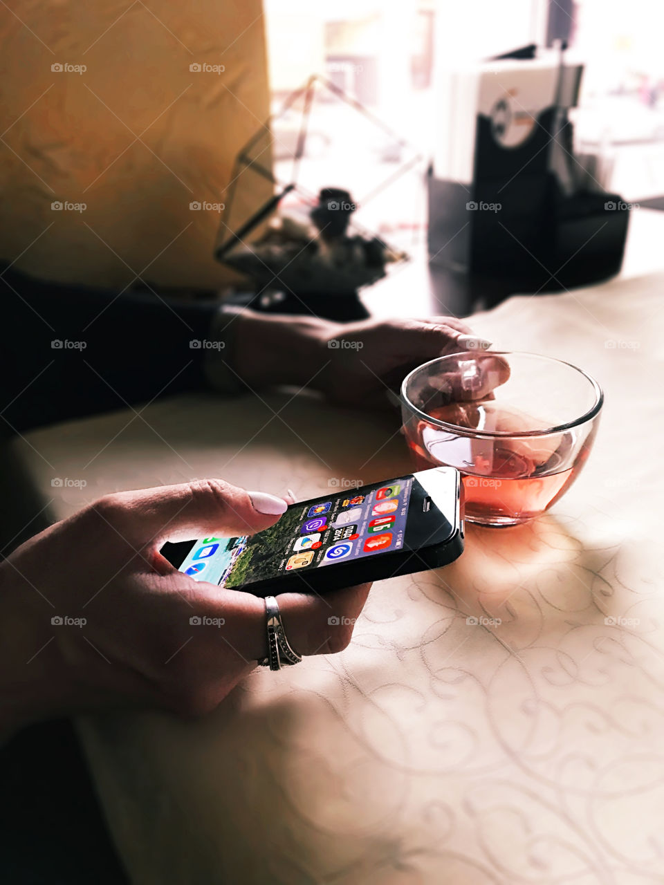 Young woman using different gadgets in her mobile phone while drinking herbal tea at the cafe 