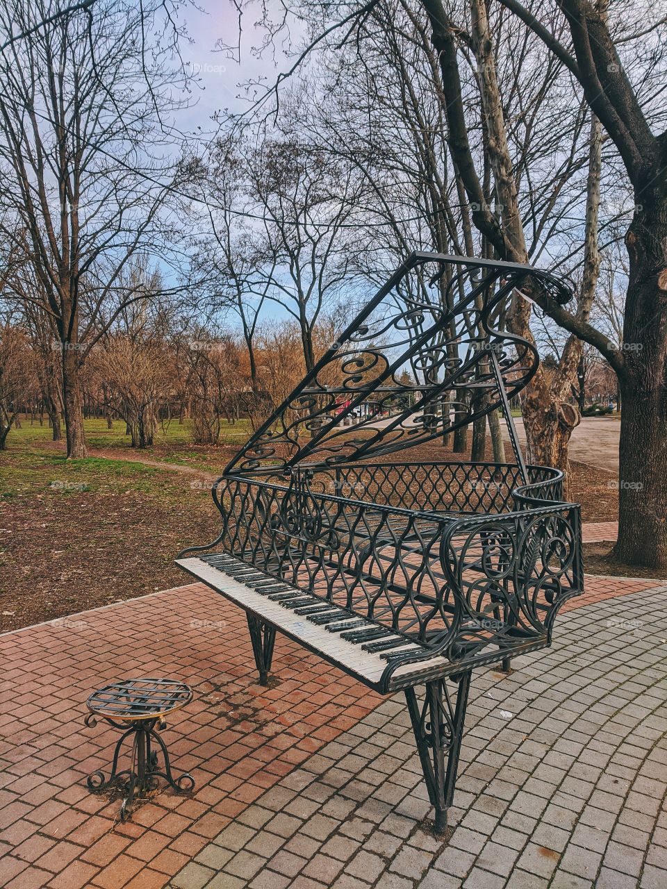 Sculpture in the city park.  Metal piano and chair in a spring park in the afternoon.