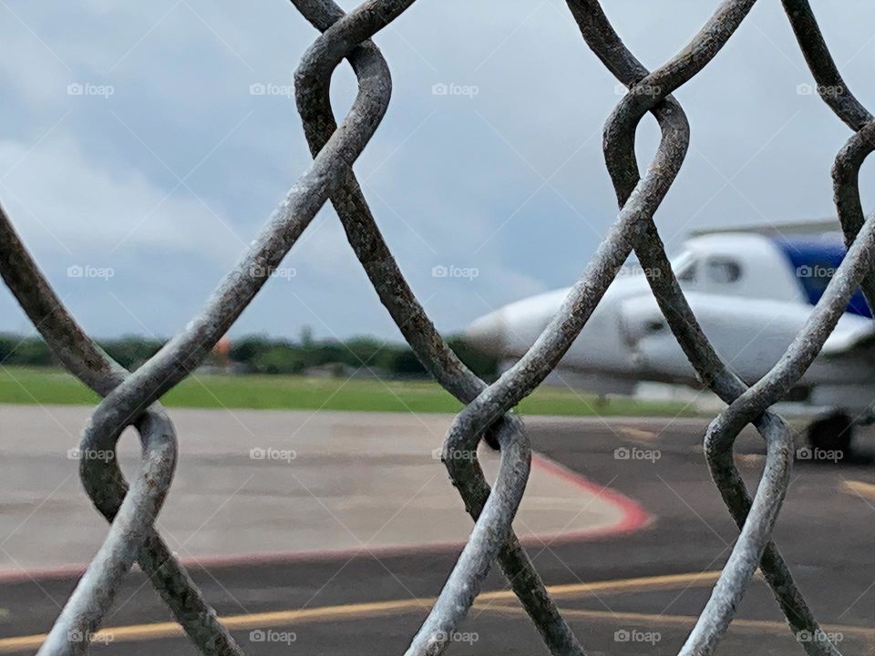 Small Airport for leisure and activities and other uses and purposes for outdoor fun and skydiving. Seeing a plane by the plane track behind a link chain fence.