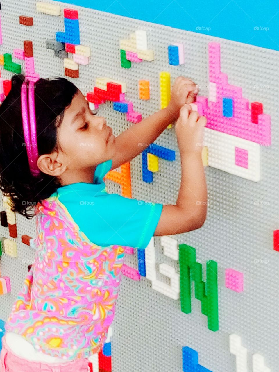 Little girl continues building lego bricks, making a pink house