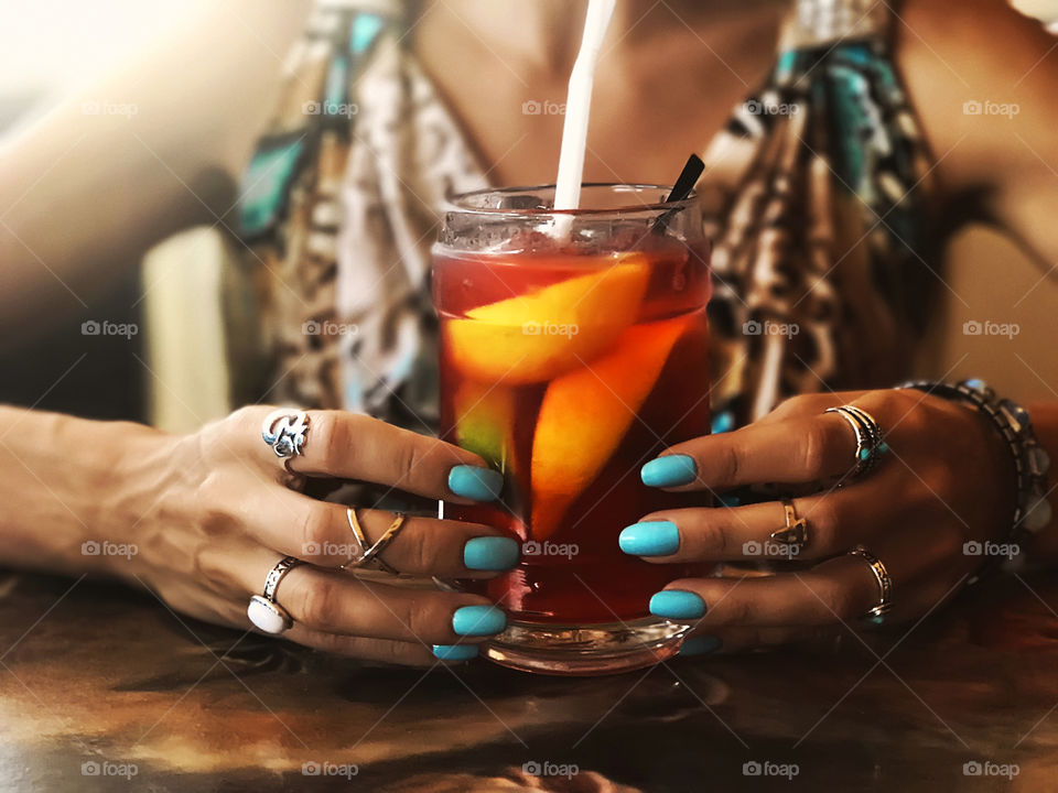 Young woman with blue manicure holding tropical cocktail with orange fruits 