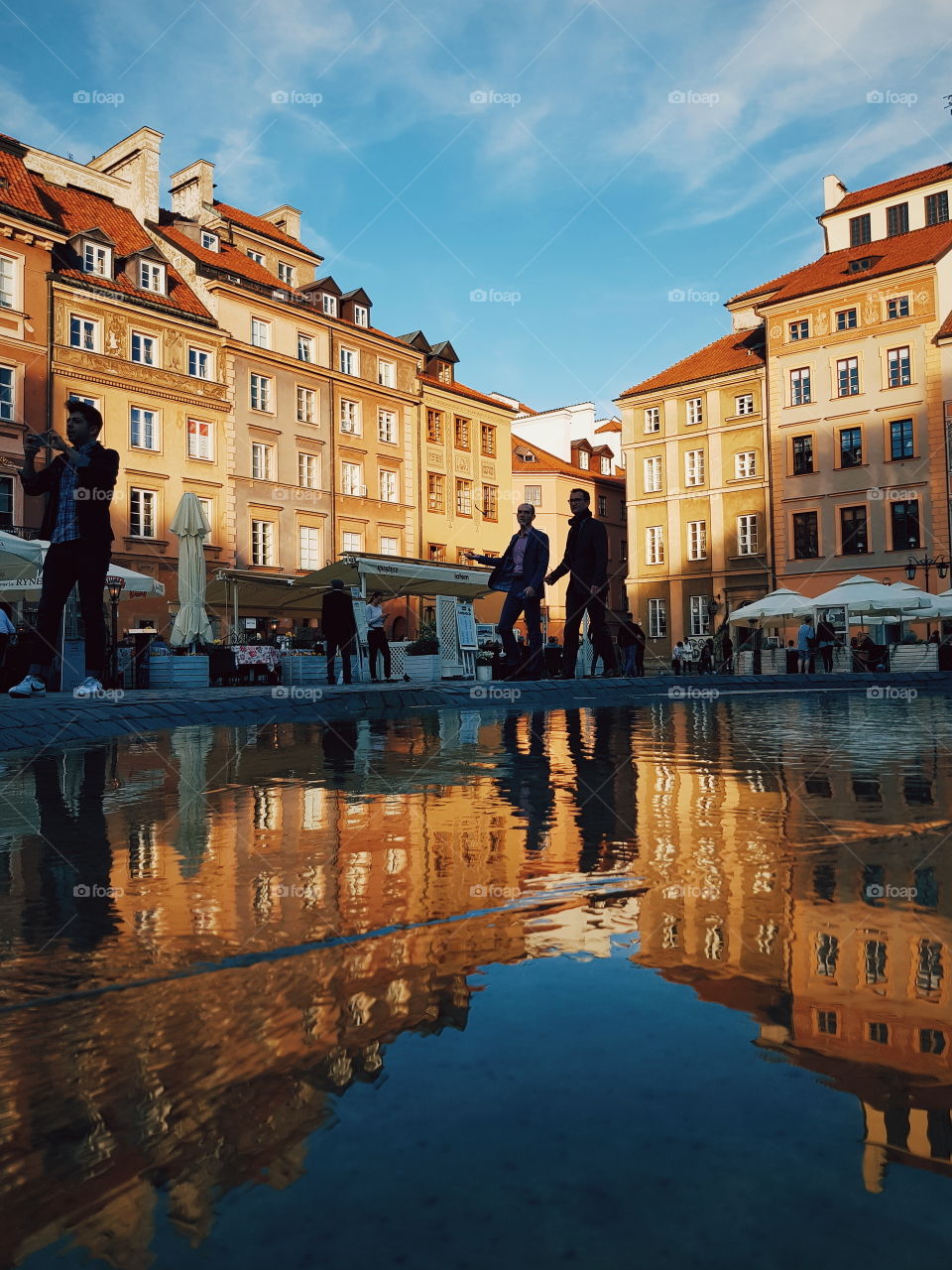 Reflection of the old market square in Warsaw with silhouettes of people passing.