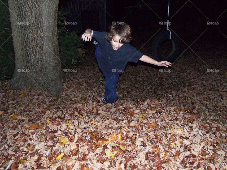 An excited little boy leaps into a leaf pile