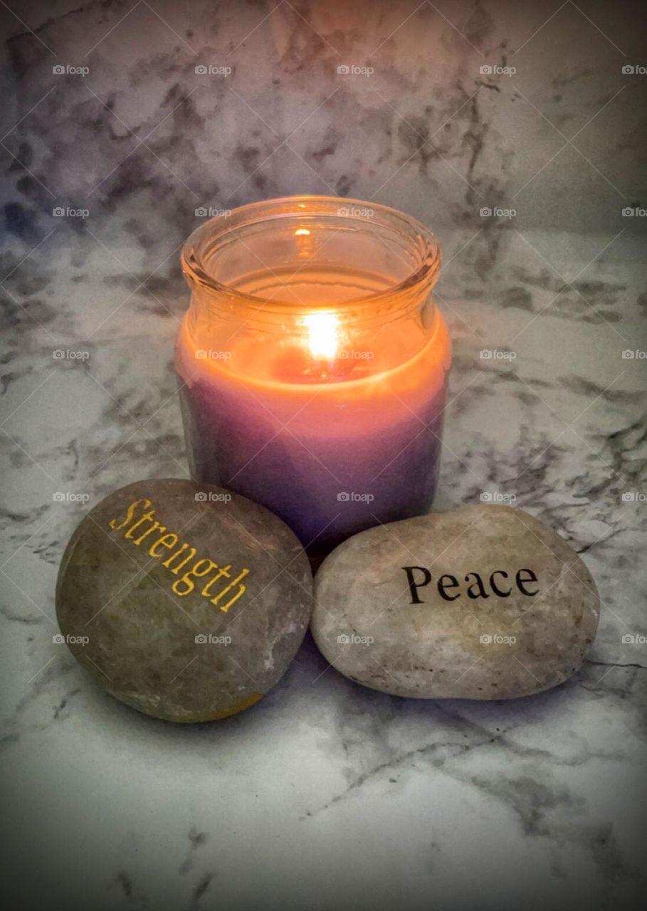 A burning candle aside rocks stating strength and peace on a marble background