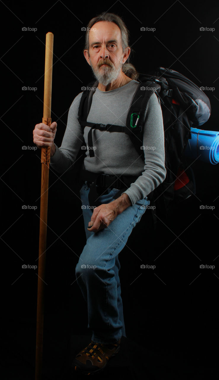 Senior beard man with stick and backpack against black background