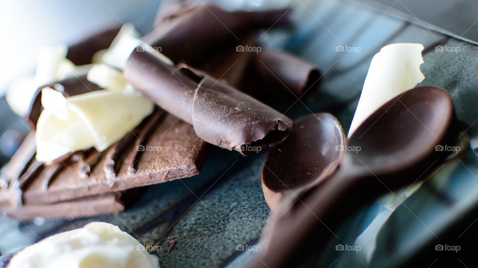 Chocolate spoons on plate with shaved white and dark chocolate curls and cookies 