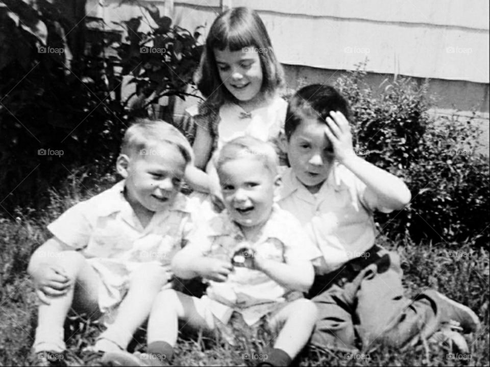 Old time black and white photo of siblings in front yard. 1950's family picture. Three brothers. One older sister.