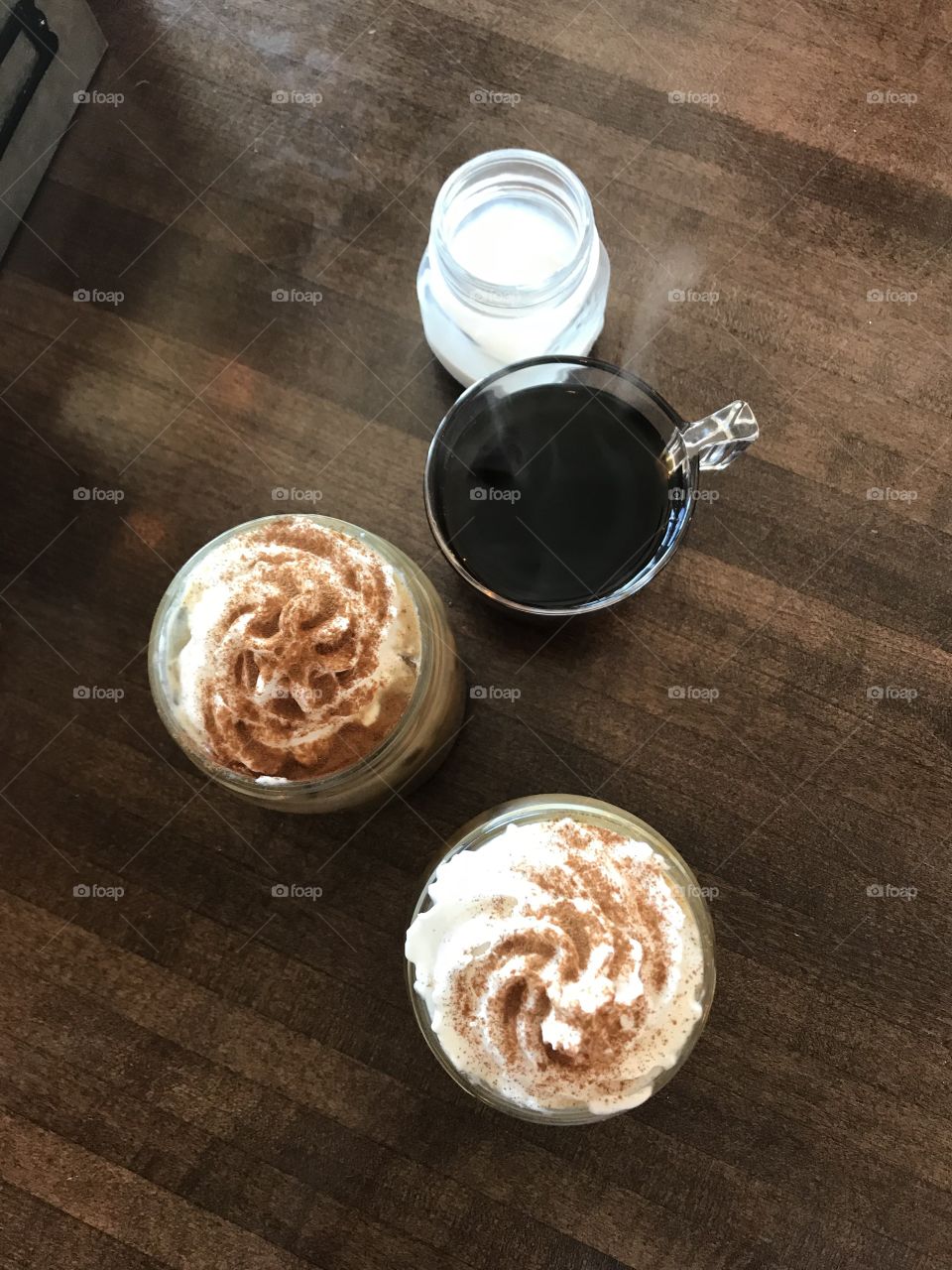 Delicious iced coffee’s with whipped cream and topping beside a steaming cup of fresh brewed coffee and cream. 