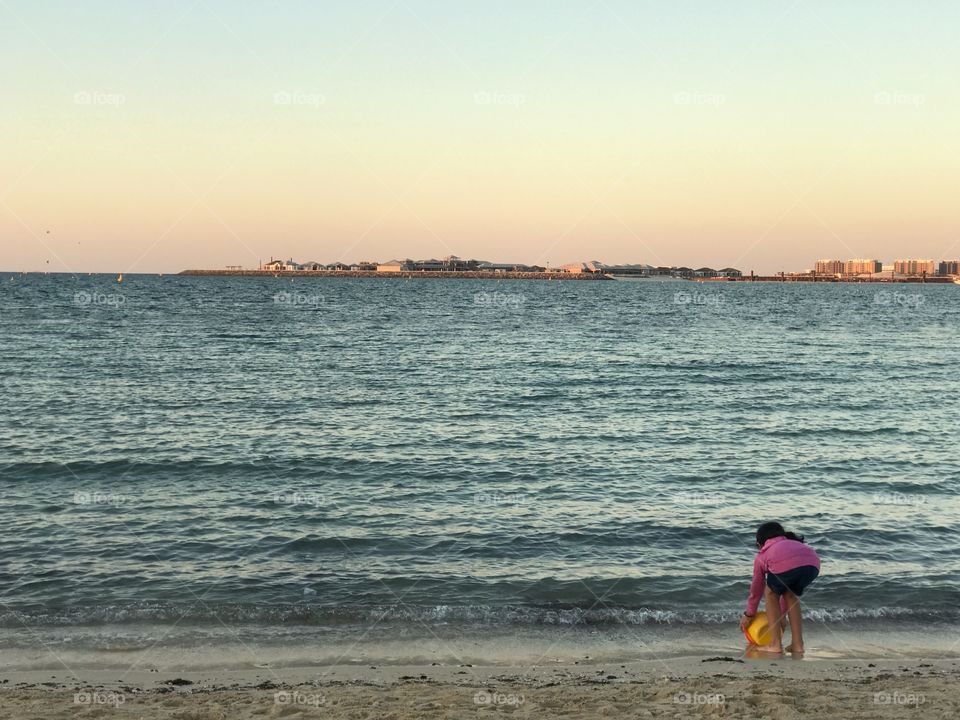 Small girl alone at the beach collecting water in the bucket to make a sand castle 