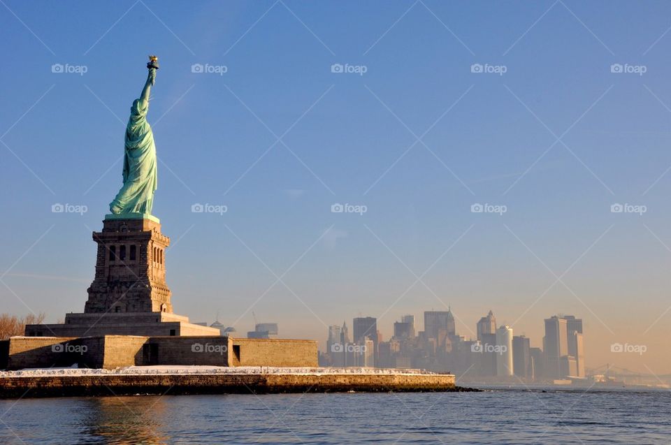 Statue of liberty with manhatan skyline on sunny day