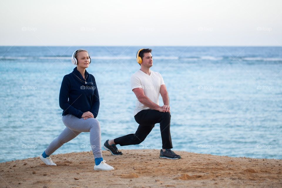 Sport . man and woman wearing headphones do exercises at dawn