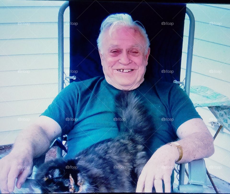 Man sitting outdoors & smiling with a cat on his lap.