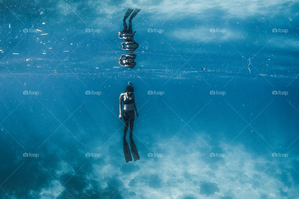A female freediver is reflected on the water surface as she floats underwater 