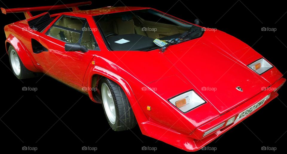 ISOLATED on BLACK,
Red Lamborghini Countach
it is a mid-engined, V12 sports car produced by Italian car manufacturer Lamborghini from 1974 to 1990. Its design pioneered and popularized the wedge-shaped, sharply angled look popular in many high-performance sports cars. It also popularized the "cab forward" design concept, which pushes the passenger compartment forward to accommodate a larger engine.
In 2004, American car magazine Sports Car International named the car number three on the list of Top Sports Cars of the 1970s, and listed it number ten on their list of Top Sports Cars of the 1980s.
Engine
The rear wheels were driven by a traditional Lamborghini V12 engine mounted longitudinally with a mid-engined configuration. This contrasted with the Miura with its centrally mounted, transversely-installed engine. For better weight distribution, the engine is pointed "backwards"; the output shaft is at the front, and the gearbox is in front of the engine, the driveshaft running back through the engine's sump to a differential at the rear. Although originally planned as a 5 L (310 cu in) powerplant, the first production cars used the Lamborghini Miura's 4-liter engine. Later advances increased the displacement to 4754 cc and then (in the "Quattrovalvole" model) 5167 cc with four valves per cylinder.
All Lamborghini Countaches were equipped with six Weber carburetors until the arrival of the 5000QV model, at which time the car became available in America, and used Bosch K-Jetronic fuel injection. The European models, however, continued to use the carburetors (producing more power than fuel-injected cars) until the arrival of the Lamborghini Diablo, which replaced the Countach.