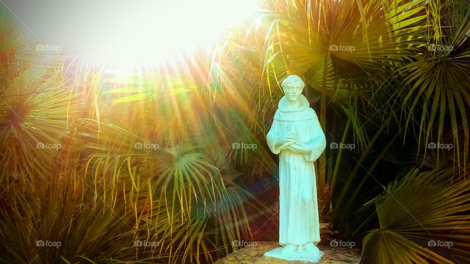 Saint Francis Of Assisi Statue with sun rays shining down on him at sunset